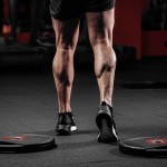 Trained man's legs with muscular calves in sneakers in fitness training gym