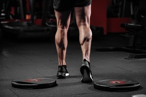 Trained man's legs with muscular calves in sneakers in fitness training gym